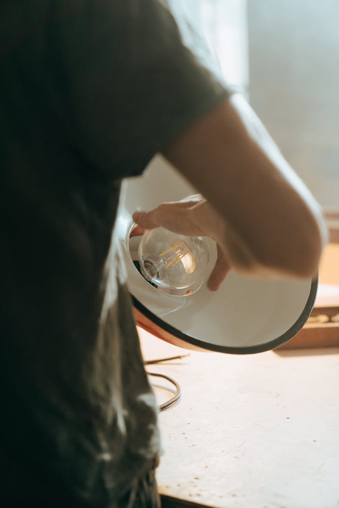 Person adjusting a vintage lightbulb inside a repair workshop setting.